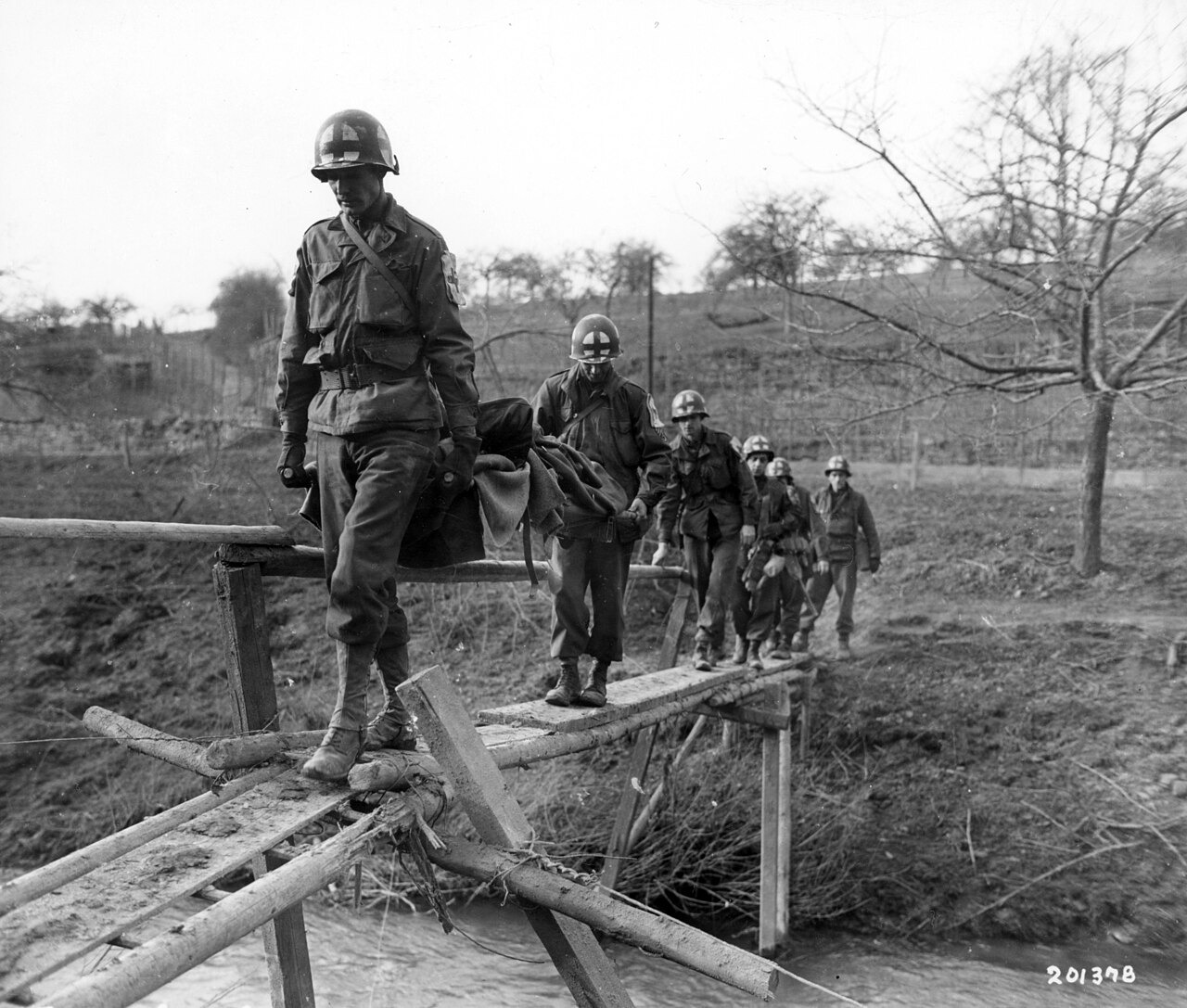 Tim medis menggotong prajurit Infanteri ke-304 yang terluka melintasi jembatan kayu di Holsthum, Jerman, Februari 1945